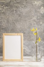 Wooden frame with yellow trout lily or dogtooth violet flowers in glass on gray concrete background