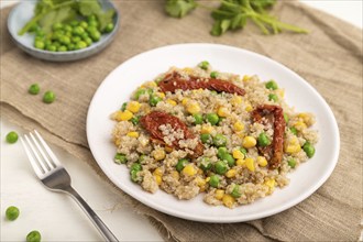 Quinoa porridge with green pea, corn and dried tomatoes on ceramic plate on a white wooden