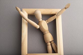 Wooden mannequin climbs out of a wooden frame with raised arms on gray pastel background. escape,