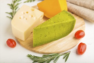 Green basil cheese and various types of cheese with rosemary and tomatoes on wooden board on a