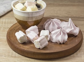 Chewing marshmallows, meringue and coffee cup on a wooden board and linen tablecloth