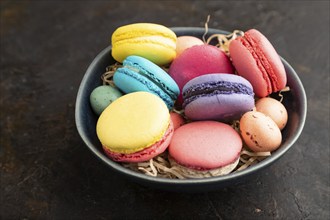 Multicolored macaroons and chocolate eggs in ceramic bowl on black concrete background. side view,