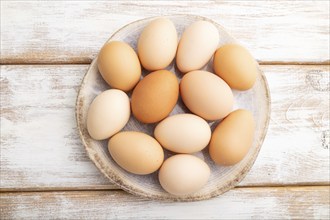 Pile of colored chicken eggs on plate on a white wooden background. top view, flat lay, close up