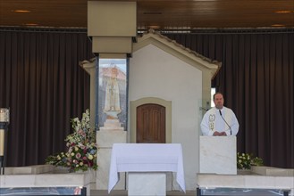 Priest standing at the altar in a small chapel surrounded by flowers, Apparition Chapel, Santuario