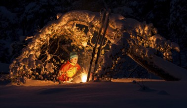 Man grilling sausage at a campfire under a snowy pine tree, Gällivare, Norrbotten, Lapland, Sweden,