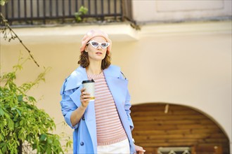 Beautiful brunette woman walks in the city with a cardboard glass of coffee in sunglasses