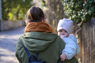 Mother holding her child with a cold and a dummy in her mouth on the way to the paediatrician