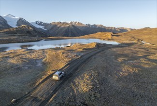 Aerial view, off-road vehicle on gravel track, mountain peak and mountain lake, evening mood,