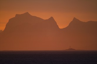 Lighthouse in front of a mountain backdrop at sunset, North Sea, Lofoten, Norway, Europe