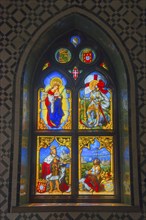 A colourful stained glass window with religious and medieval scenes, depicted in a Gothic stained