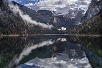 The Vordere Gosausee in autumn. In the background, the Dachstein mountain range in clouds. Partly