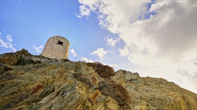 Ruin of a windmill, Old tower on a rocky hill in front of a cloudy sky, Colourful mountain village,