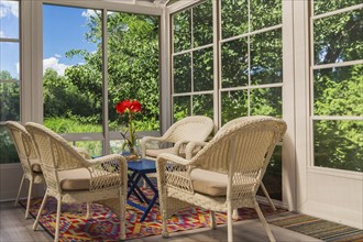 Beige wicker armchairs and blue wooden table in sunroom at back of luxurious residential home,