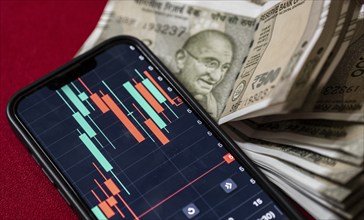 Stock market graph or chart display on a mobile phone against Indian 500 rupee paper currency note