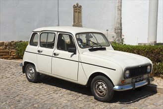 White vintage car on cobblestones in front of a historic building, Renault 4, R4, Tavira, Faro,