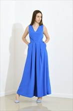 Full length portrait of stylish trendy woman in blue long sleeveless dress holding her hands in