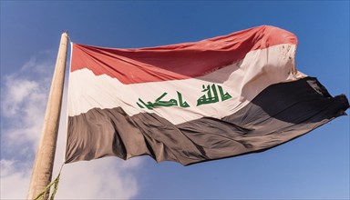 The flag of Iraq flutters in the wind, isolated against a blue sky