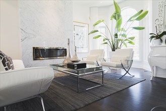 Living room with white leather and chrome sofa, armchairs, glass-top coffee table, gas fireplace