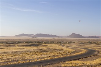 Landscape in arid environment with a road, mountains in the background and a hot air balloon in the