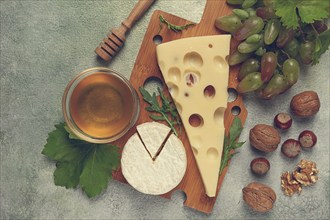 Cheese with big holes, emmental, maasdam, brie cheese, on a cutting board, with grapes and honey,