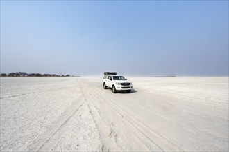 Four-wheel drive Toyota Hilux with roof tent, driving over salt pan, lone car in large wide plain,