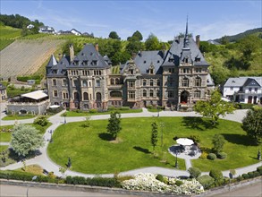 Historic castle with well-tended garden, surrounded by green hills under a blue sky in summer,