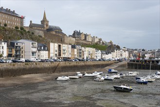 Coastal town with harbour and boats at low water level in front of historic architecture under a