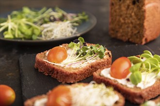 Red beet bread sandwiches with cream cheese, tomatoes and microgreen on black concrete background.