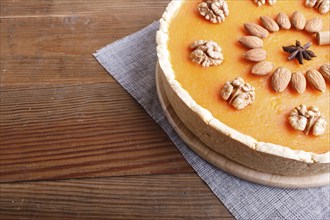 Traditional american sweet pumpkin pie decorated with nuts, on brown wooden background. close up,