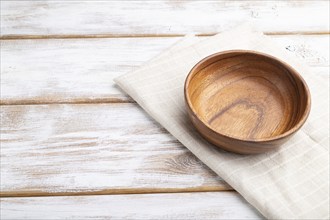 Empty wooden bowl on white wooden background and linen textile. Side view, close up, copy space