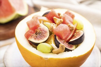 Vegetarian fruit salad of watermelon, grapes, figs, pear, orange, cashew on white wooden background