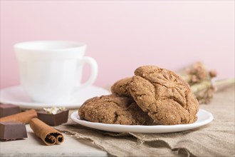 Homemade oatmeal cookies with a cup of cocoa on a linen textile and pink pastel background. side