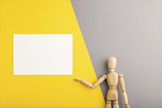 Wooden mannequin holding white blank poster on gray and yellow pastel background. copy space,