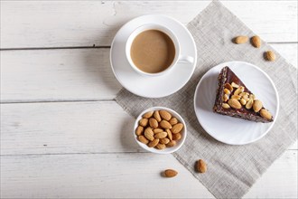 Chocolate cake with caramel, peanuts and almonds on a white wooden background. cup of coffee, top