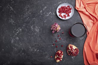 Glass of pomegranate juice on a black concrete background with red textile. Top view, copy space,