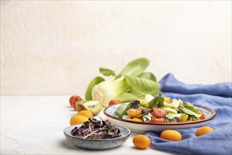 Vegetarian salad of pac choi cabbage, kiwi, tomatoes, kumquat, microgreen sprouts on a white