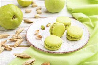 Green macarons or macaroons cakes with cup of coffee on a white wooden background and green linen