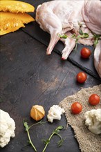 Whole raw rabbit with pumpkin, tomatoes, pea sprouts on a black concrete background and linen