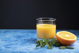 Glass of orange juice with mint on a black and blue background. Hard light, contrast. Side view,