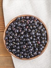 Fresh black currant in wooden bowl on wooden background. top view, flat lay, close up