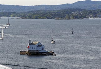 Small lighthouse on an island in the water, surrounded by boats and hills in the distance, Dyna