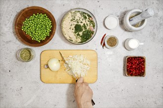 Unrecognizable man cutting fresh onion on wooden chopping board, top view