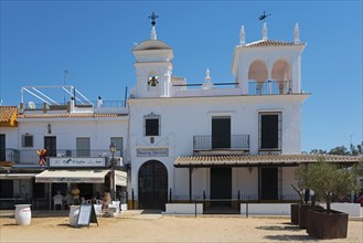 Weißes Gebäude mit Glockenturm und Straßencafé unter blauem Himmel, Wallfahrtsort, Kirche, El