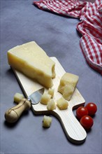 A piece of Parmesan cheese and chopped pieces of cheese on a wooden board