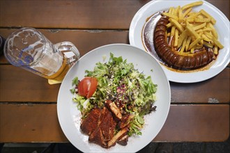 Salad with turkey strips and currywurst with French fries served in a garden withe, Bavaria,