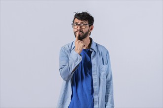 Pensive young man with finger on his lips on an isolated background. Worried guy with finger on his