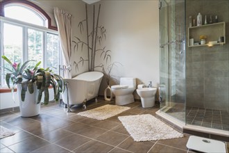 Freestanding bathtub, bidet, clear glass shower stall in en suite with grey nuanced ceramic tile