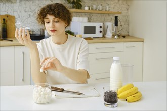 Woman takes out a piece of sugar from a sugar bowl while sitting at kitchen table