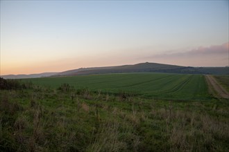 Chalk downland landscape at dusk with red sky from setting sun view to Milk HiIl, Alton Barnes,