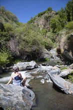 Woman sitting on rock by rapids in the channel of the River Rio Poqueira gorge valley, High